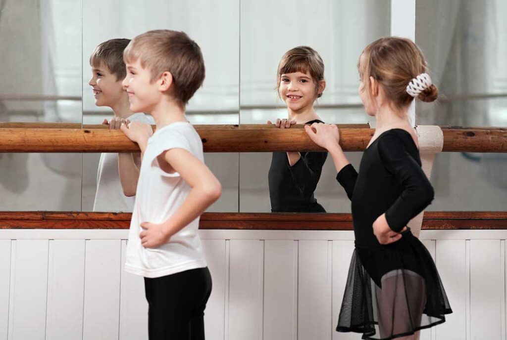 A group of young children in dance attire following an instructor in a brightly lit studio.
