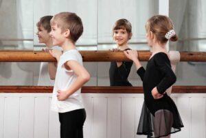 A group of young children in dance attire following an instructor in a brightly lit studio.