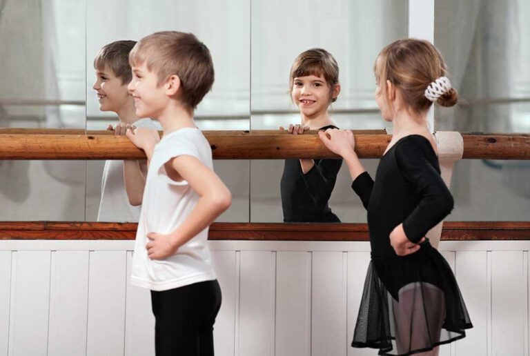 A group of young children in dance attire following an instructor in a brightly lit studio.