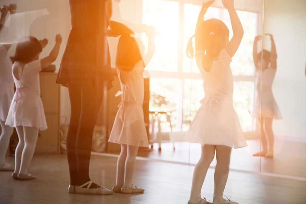 Young dancers practice a routine together in a bright studio while an instructor guides their movements.