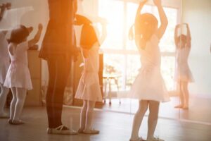 Young dancers practice a routine together in a bright studio while an instructor guides their movements.