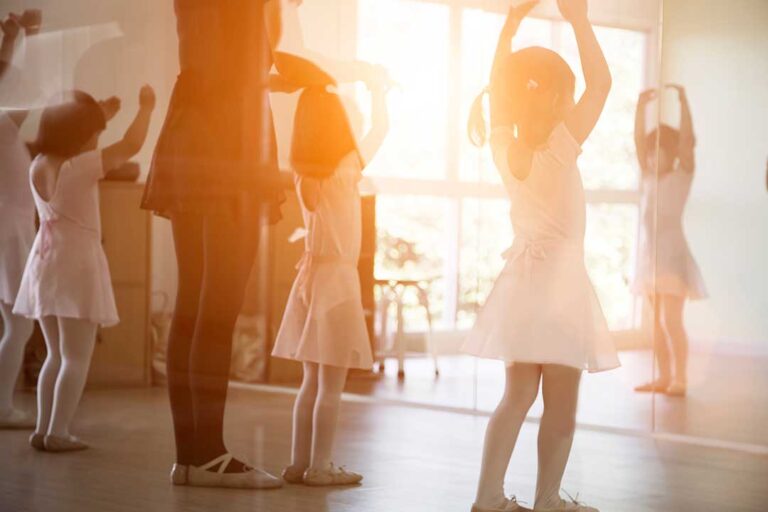 Young dancers practice a routine together in a bright studio while an instructor guides their movements.