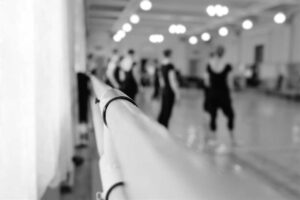 A group of young children in dance attire stretching and smiling in a bright studio with mirrors in the background.